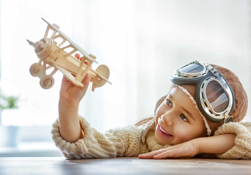 小女孩带着护目镜趴在桌子上玩飞机模型