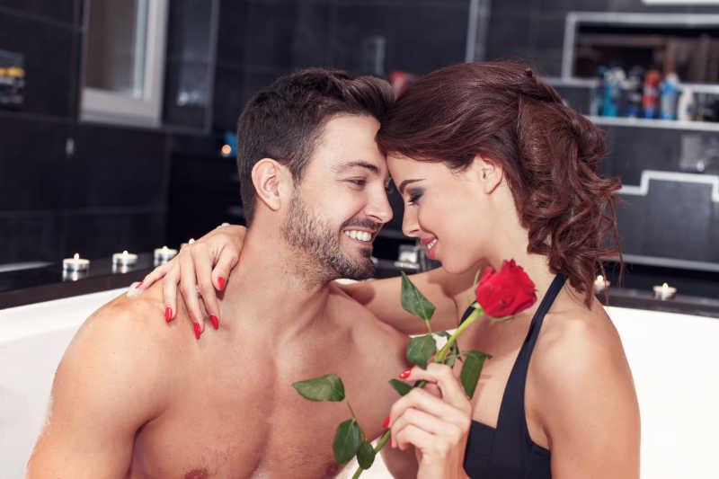 幸福的年轻夫妇拿着玫瑰在按摩浴缸里