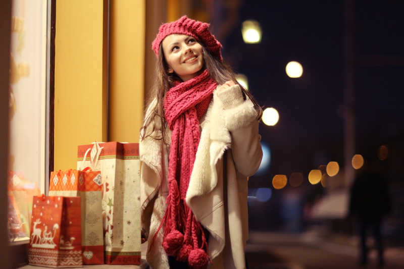 城市街头带着红色帽子和毛巾的美丽女孩身边放着购物袋