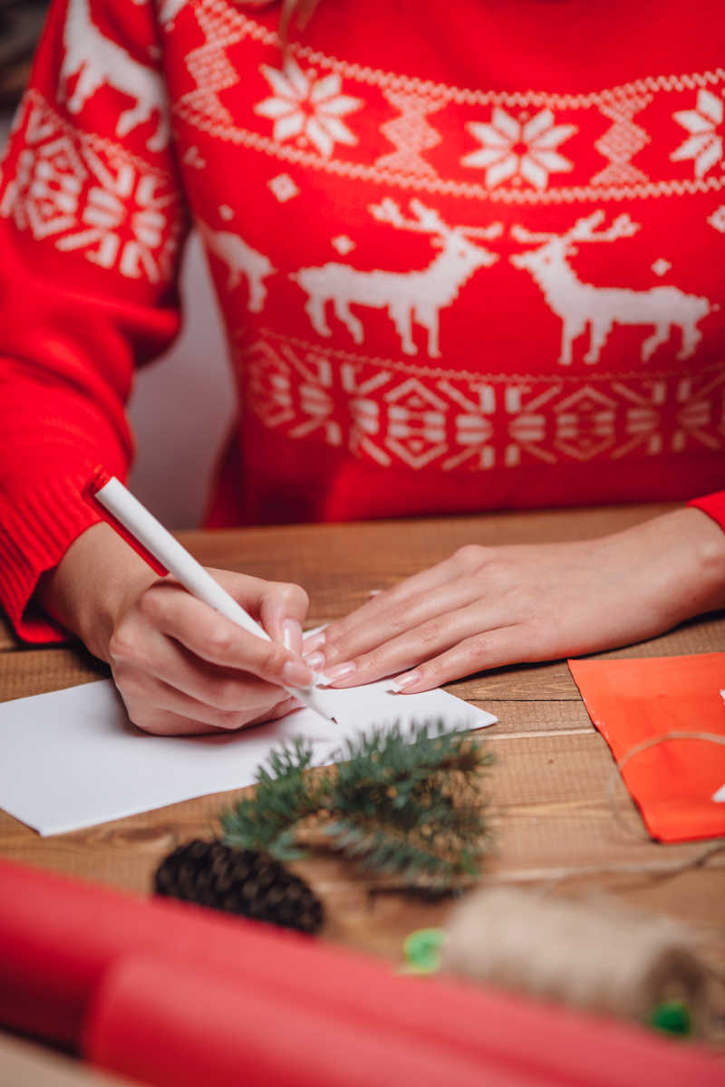 红色圣诞毛衣的女人在写圣诞明信片