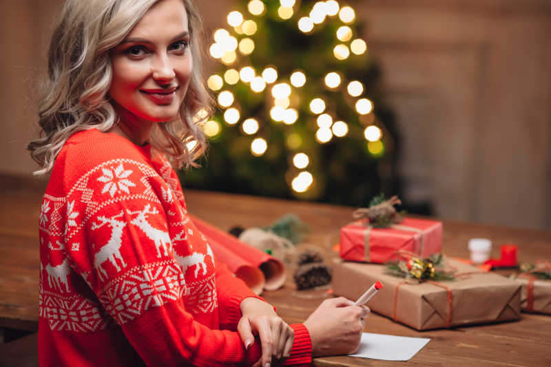 穿着红色毛衣的金发女郎在圣诞明信片上写字