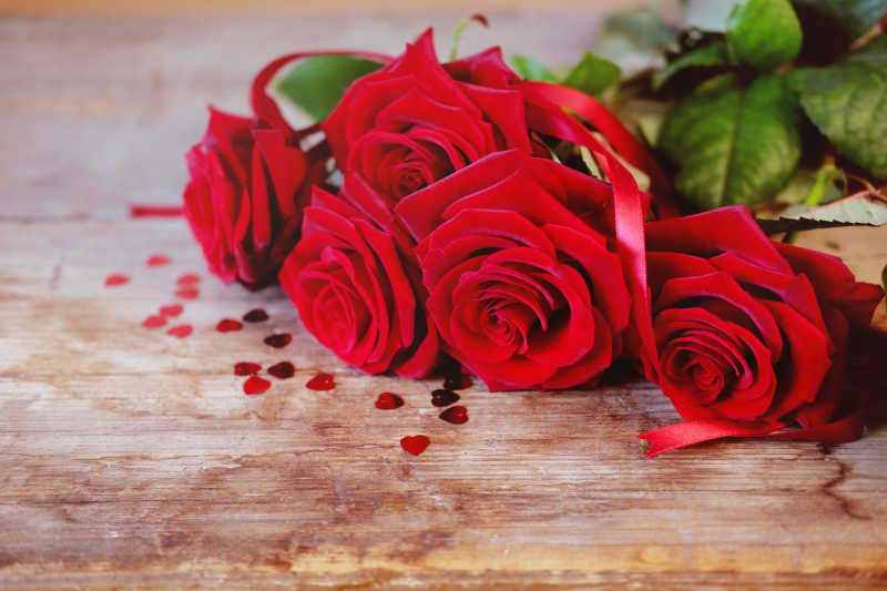 木桌上的红玫瑰花束和丝带