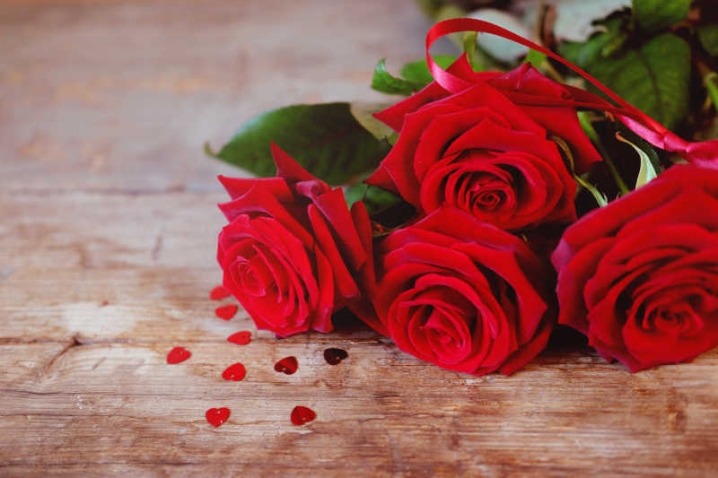 木桌上红色的玫瑰花和散落的心形剪纸