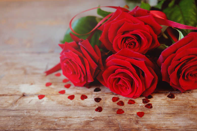 木桌上用红色丝带绑着的红色玫瑰花束
