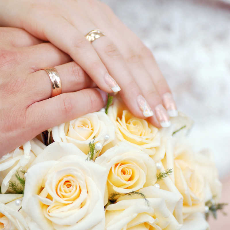 在黄色的玫瑰花上的新娘和新郎的手
