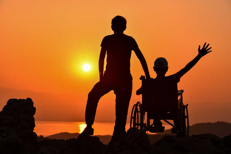 坐在轮椅上的人和站着的人欣赏日落