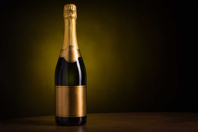 深色背景的木桌上摆一瓶空白金色标签的香槟酒
