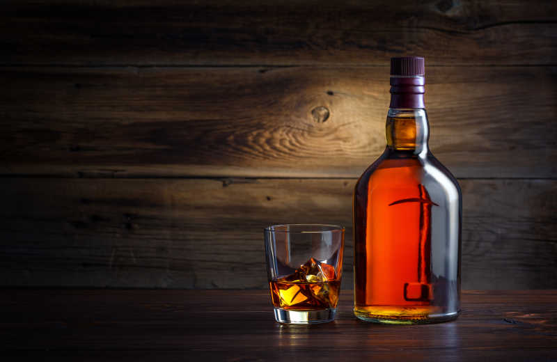 木质背景上一杯加冰的威士忌和一整瓶威士忌酒