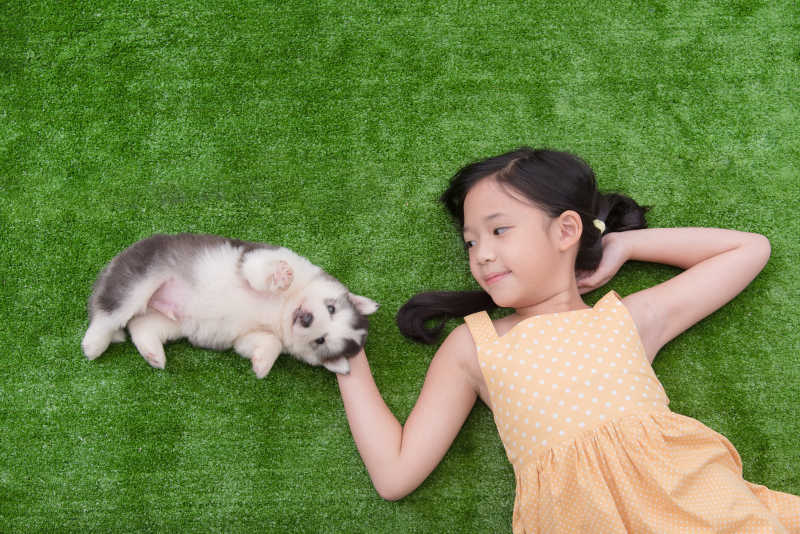 亚洲女孩和她的小狗躺在草地上玩耍