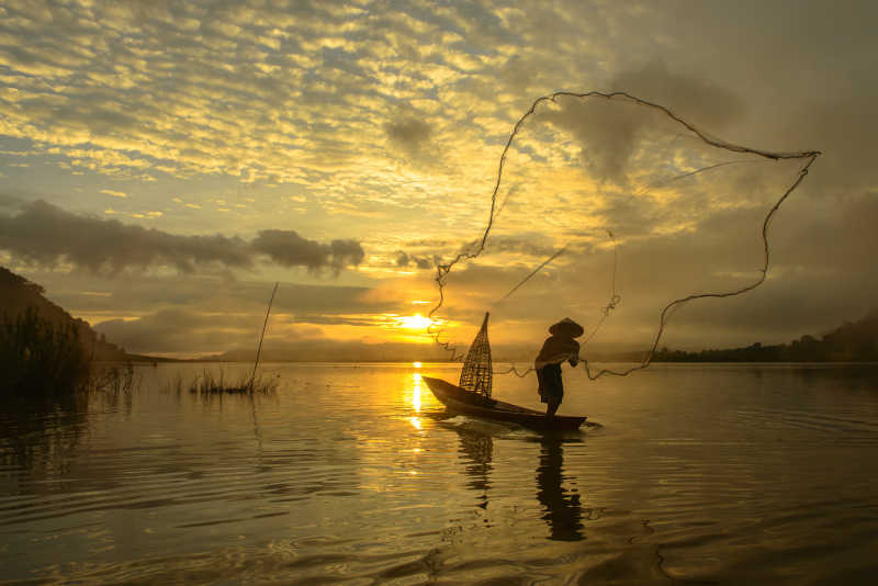 黄昏下渔夫向湖面撒网的剪影
