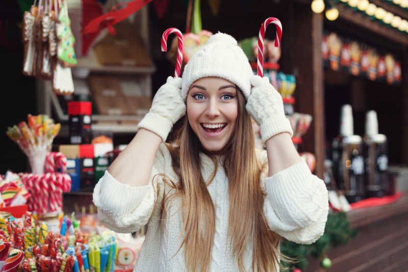 微笑开朗的年轻女人玩糖果的圣诞集市街的肖像
