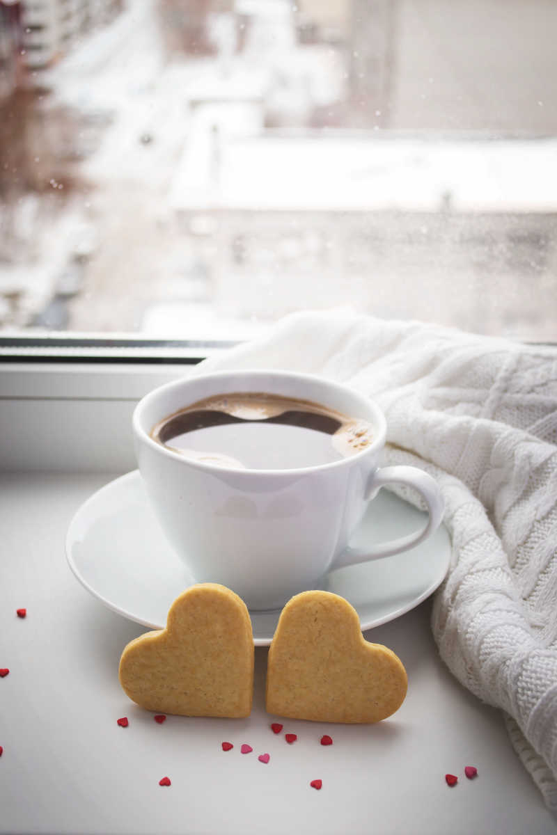 窗户前一杯咖啡和一对心形饼干