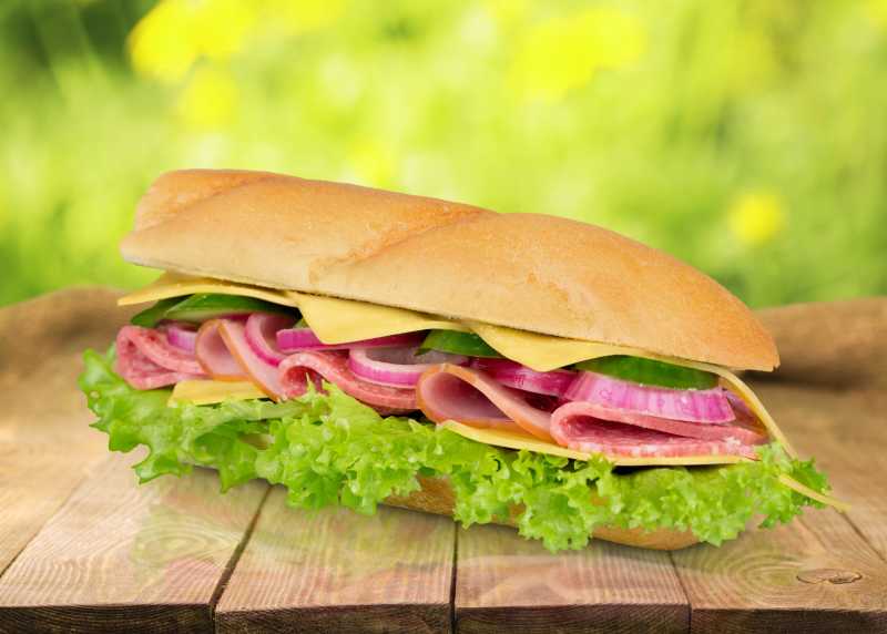 虚化绿色背景下木板上的夹肉三明治