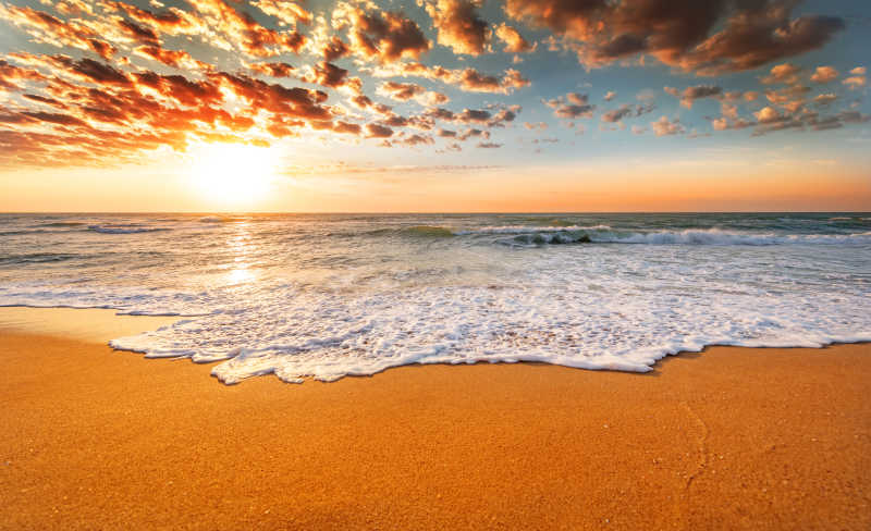 日出-日落时天空中金色的云金色的沙滩和白色的海浪