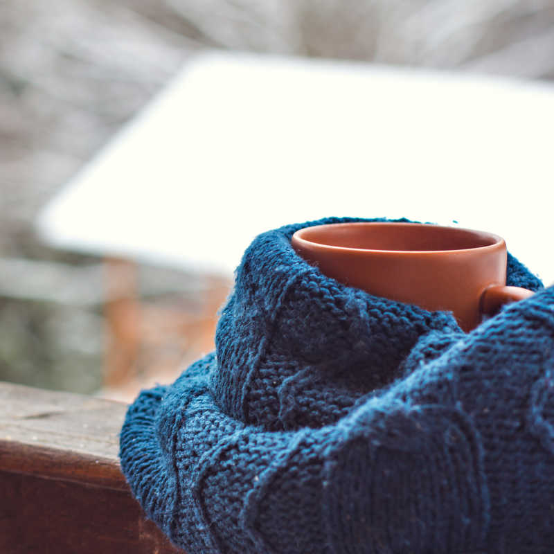 户外冬季背景下蓝色针织衫包裹着一只橘色的杯子