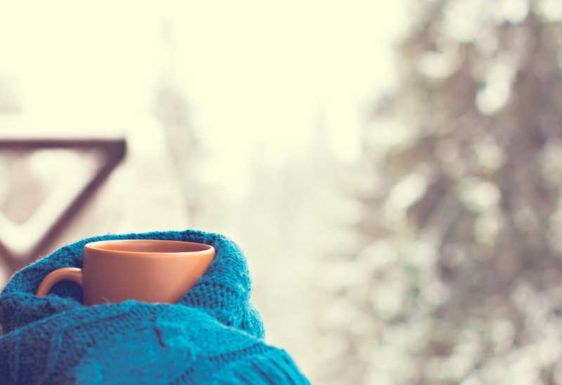 冬季户外景观背景下蓝色针织衣服包着橘色杯子