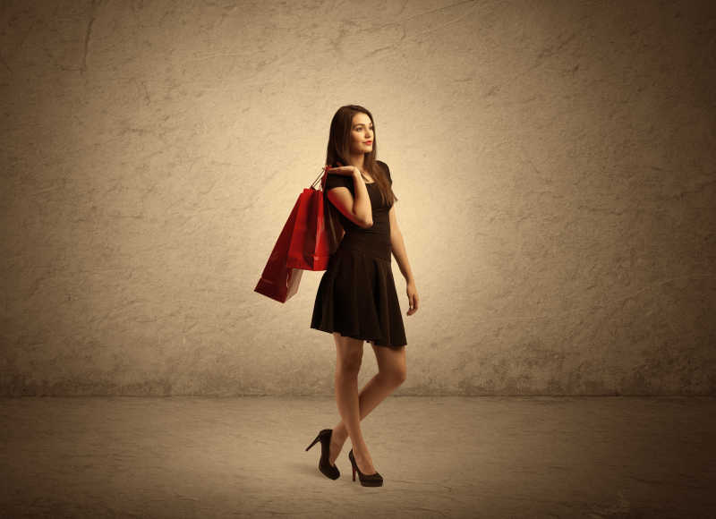一个红色的购物袋的年轻漂亮的女孩站在空空的乌贼城市墙背景概念前