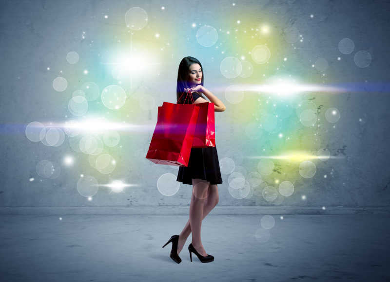 一个长头发和红色的购物袋的年轻漂亮的女孩站在彩光散景墙背景前
