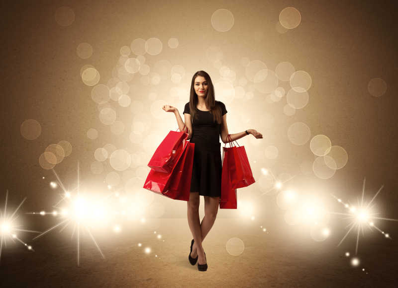一位美丽的黑衣女子拿着红色的购物袋站在棕色的背景下