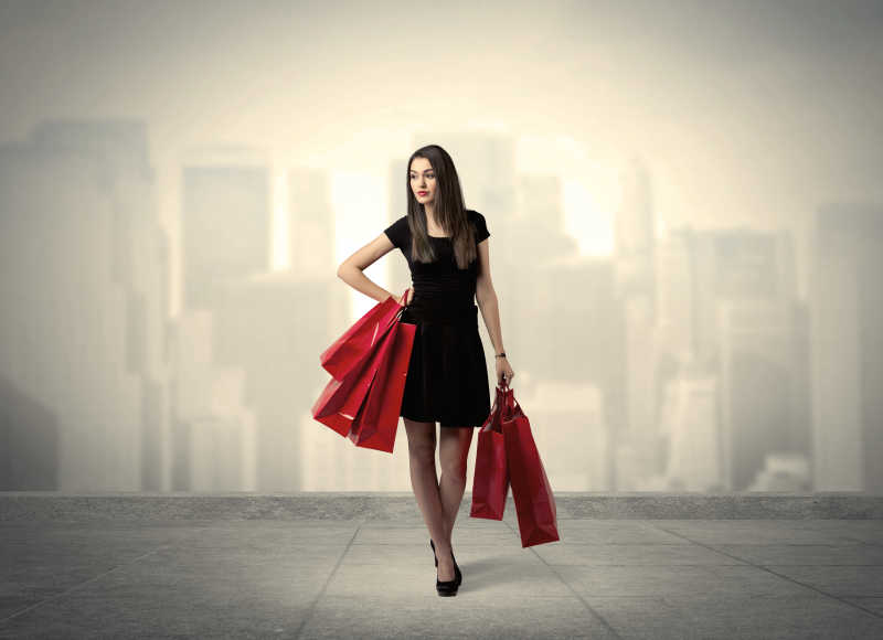 一个时尚的女性站在红色的购物袋在平台和城市景观