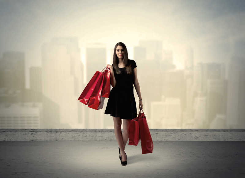 黑衣美女手持红色购物袋站在城市景观前