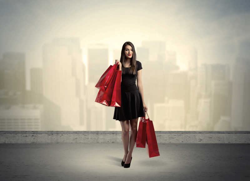 黑衣美女手持红色购物袋站在城市景观前面