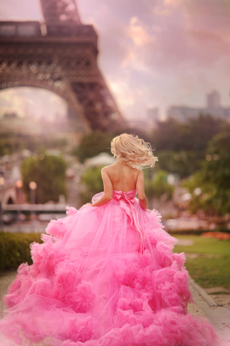 一个穿着粉红色连衣裙的女孩跑在艾菲尔铁塔的背景上