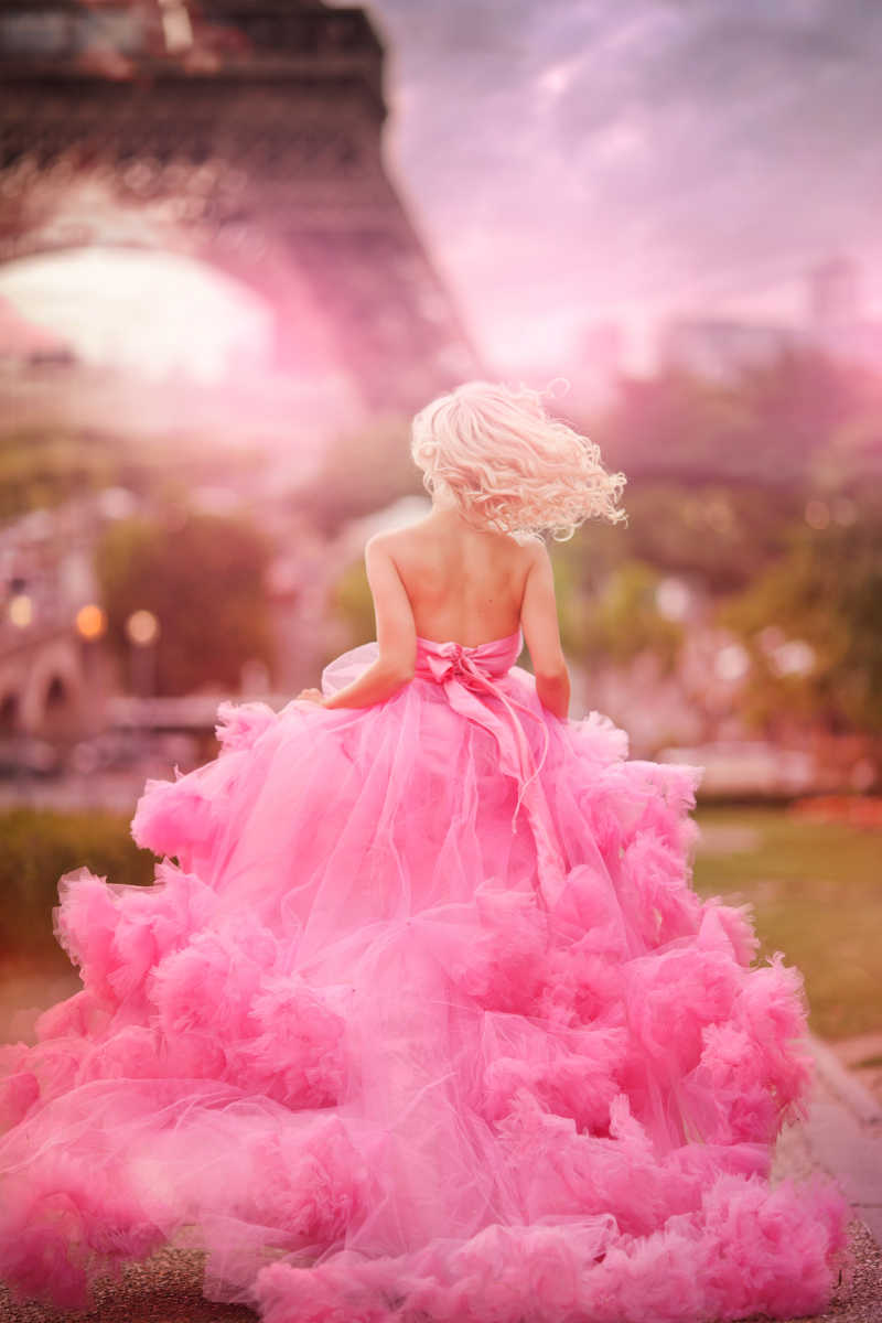 穿着粉红色连衣裙的漂亮女孩在艾菲尔铁塔下奔跑