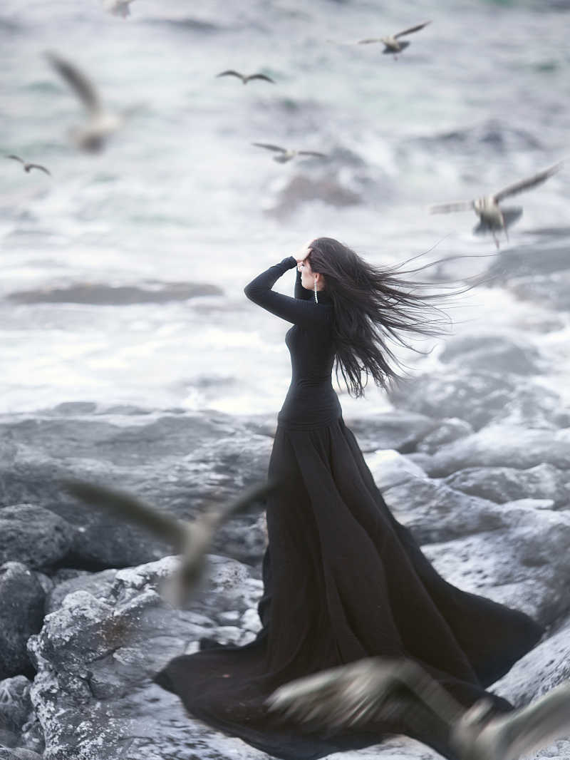 穿黑色长裙的时尚美女站在海边