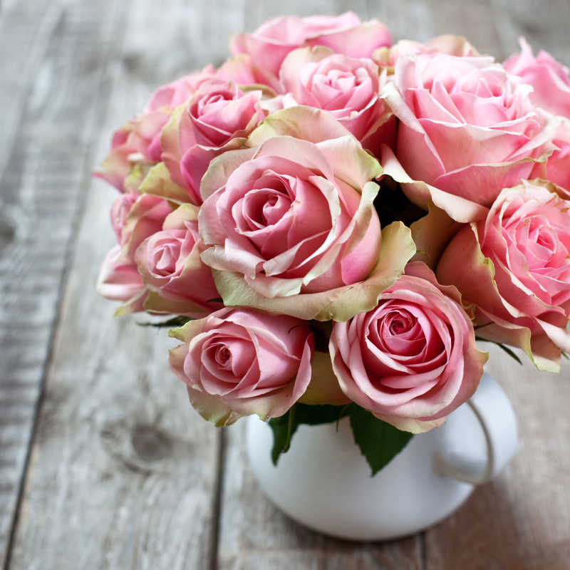 木质桌面上白色花瓶里的一束粉色玫瑰花