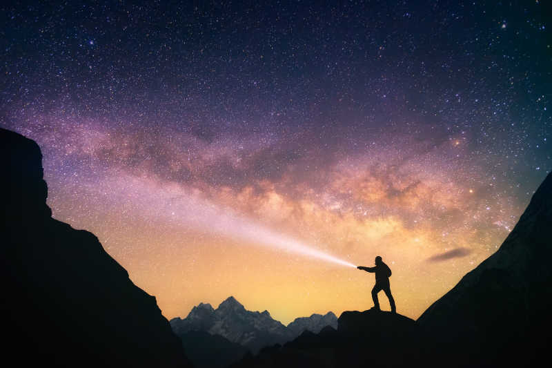 手持手电的男人站在山上的银河夜空里