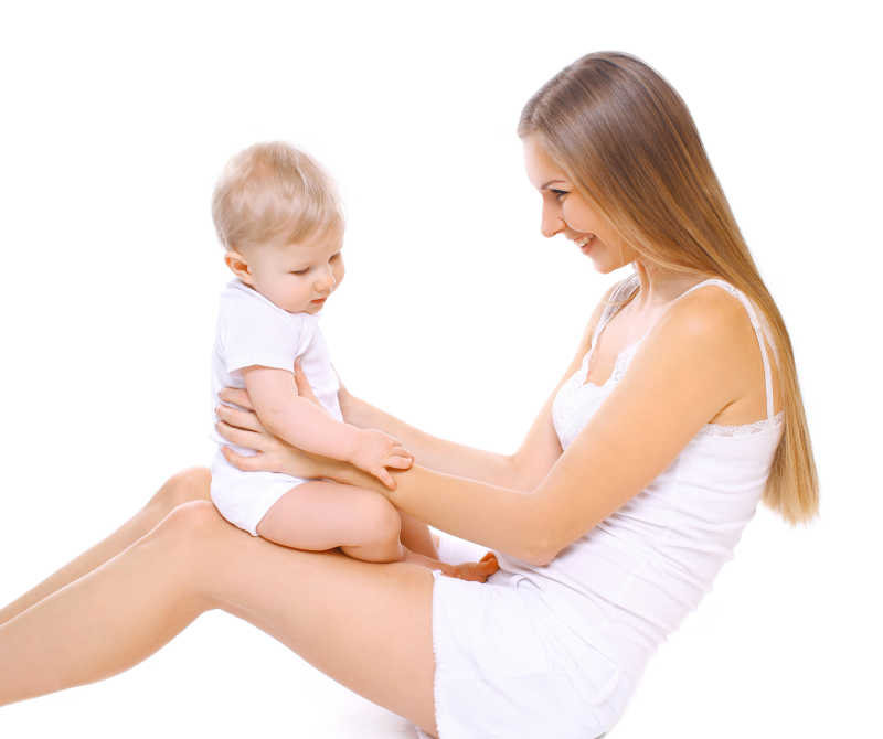 白色背景下坐在母亲的腿上玩耍的小婴儿