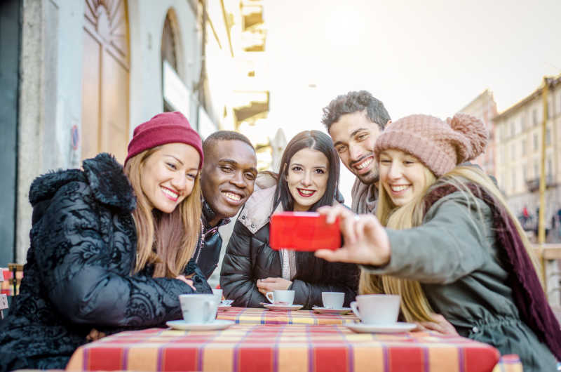 一群不同种族的朋友在户外咖啡店用手机自拍合影