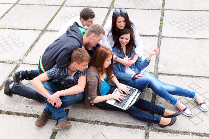一群年轻的男女围坐在一个使用笔记本电脑的女孩身边