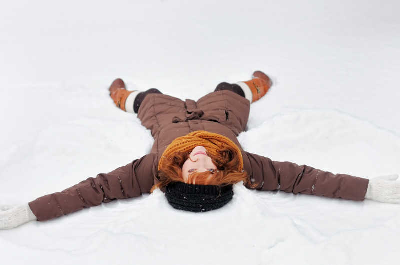 年轻的女孩躺在雪中玩耍