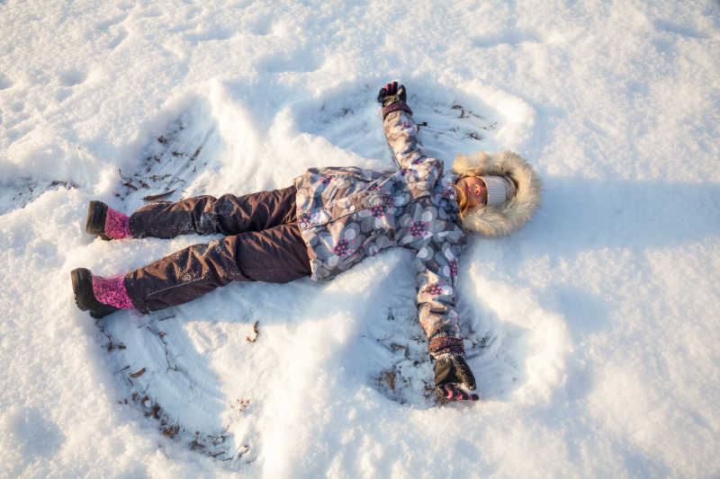 穿着温暖的冬衣躺在雪中的快乐女孩