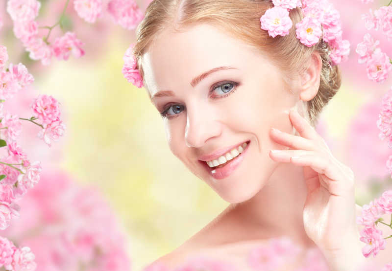 美丽的女人微笑着与头发上的粉红色的花朵