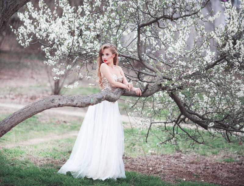 年轻漂亮的女子把手搭在盛开的桃花树上