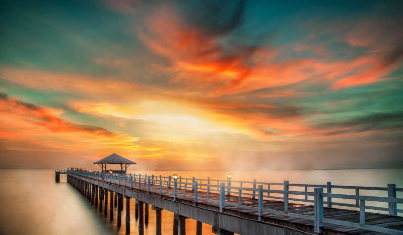 日出-日落金色天空背景下水面上的木制桥梁