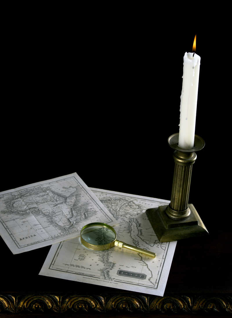 旧书桌上的蜡烛旧地图和放大镜