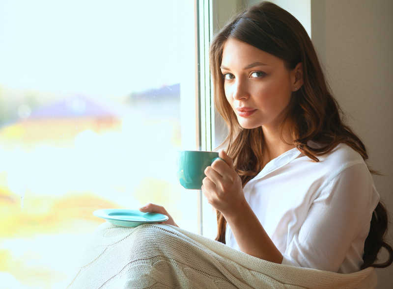 年轻女子坐在窗边喝咖啡