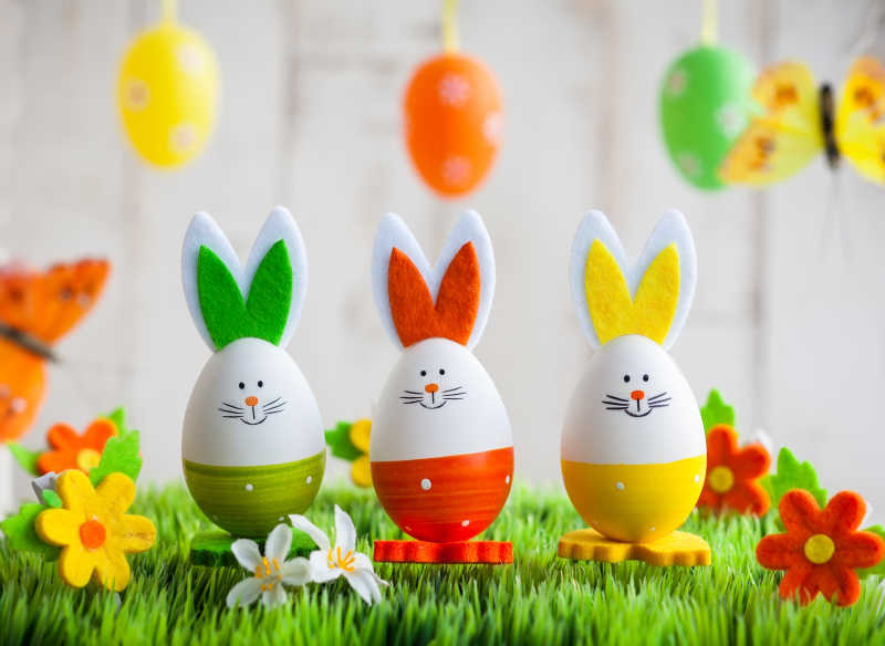 灰白色背景下绿色草地上的复活节的彩色兔子
