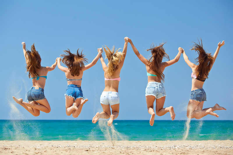 海滩上手拉手放松跳跃的青少年女孩