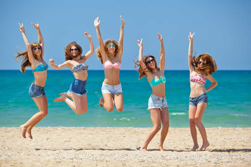 年轻女孩们在海滩上举起双手跳跃放松