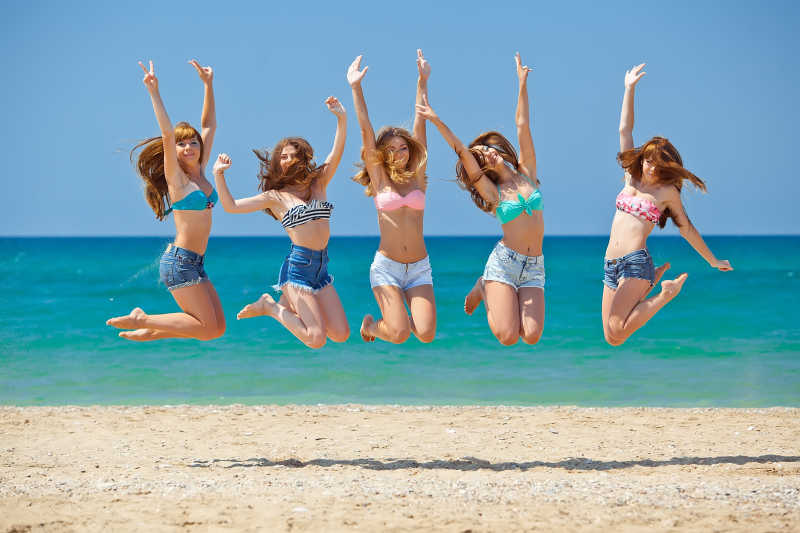 快乐跳跃的年轻女孩们在海滩上放松玩耍