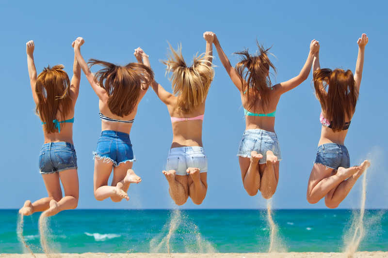 在海滩上手拉手跳起来的年轻女孩们