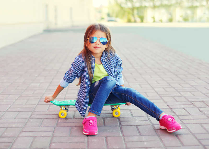 戴着墨镜和格子衬衫坐在滑板上的时尚小女孩