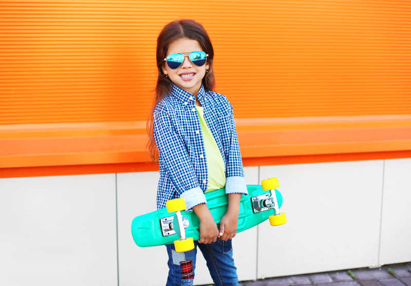 橙色背景墙上的时尚小女孩手拿滑板