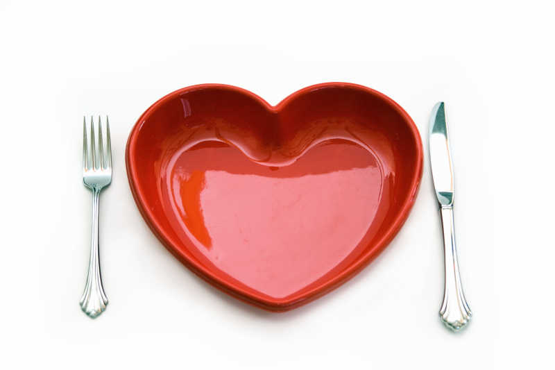 白色背景下表示心脏健康概念的心形盘子和刀叉