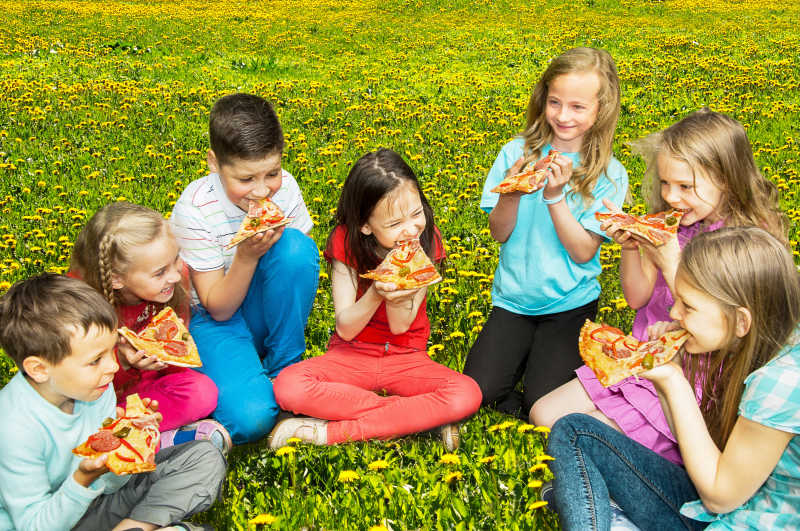 一群坐在草坪上吃着披萨的孩子们